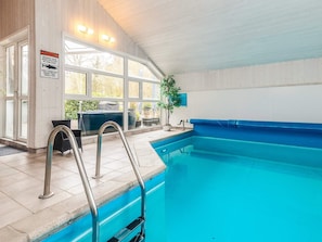 En indendørs swimmingpool med glasvægge, et metalgelænder og et fareskilt med hajer.