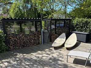 A wooden deck with a pergola, a stack of firewood, and outdoor furniture. - 5 Star Holiday Home in Gilleleje (Gilleleje)