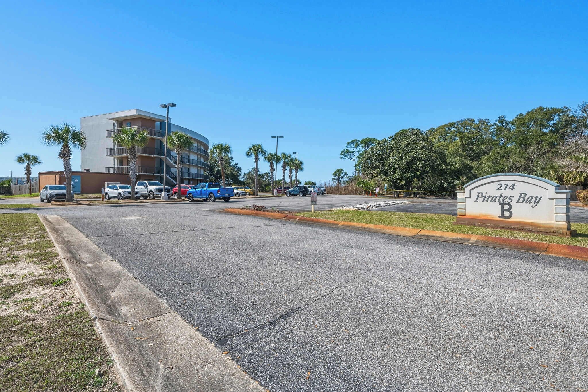 A multi-story building with a parking lot, palm trees, and a sign reading '214 Pirates Bay B'.