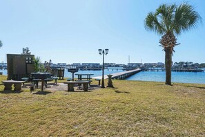 Un parque frente al agua con mesas de picnic, una palmera y un muelle que se adentra en el agua.