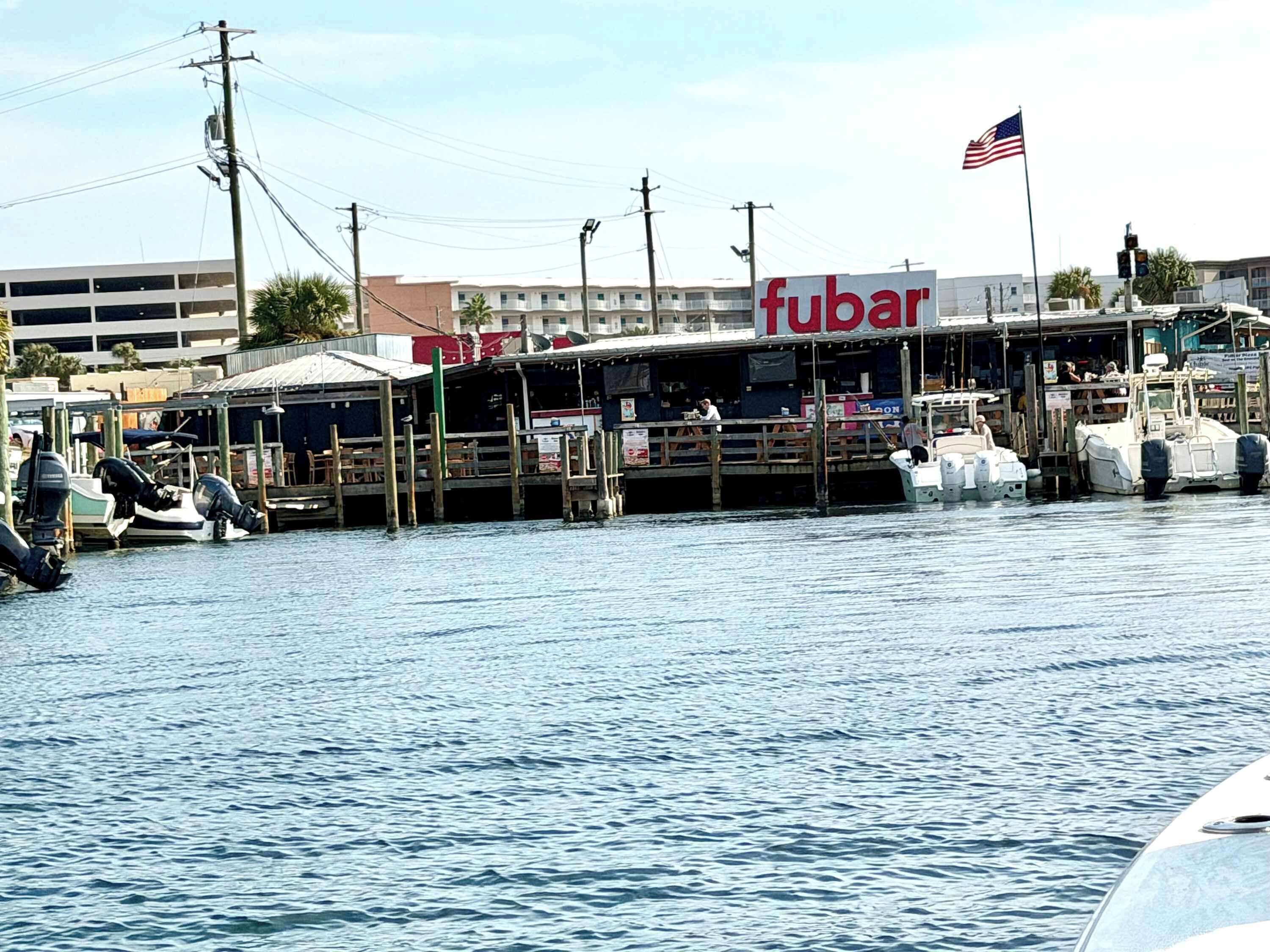 A waterfront establishment with a prominent 'fubar' sign, docked boats, and an American flag.
