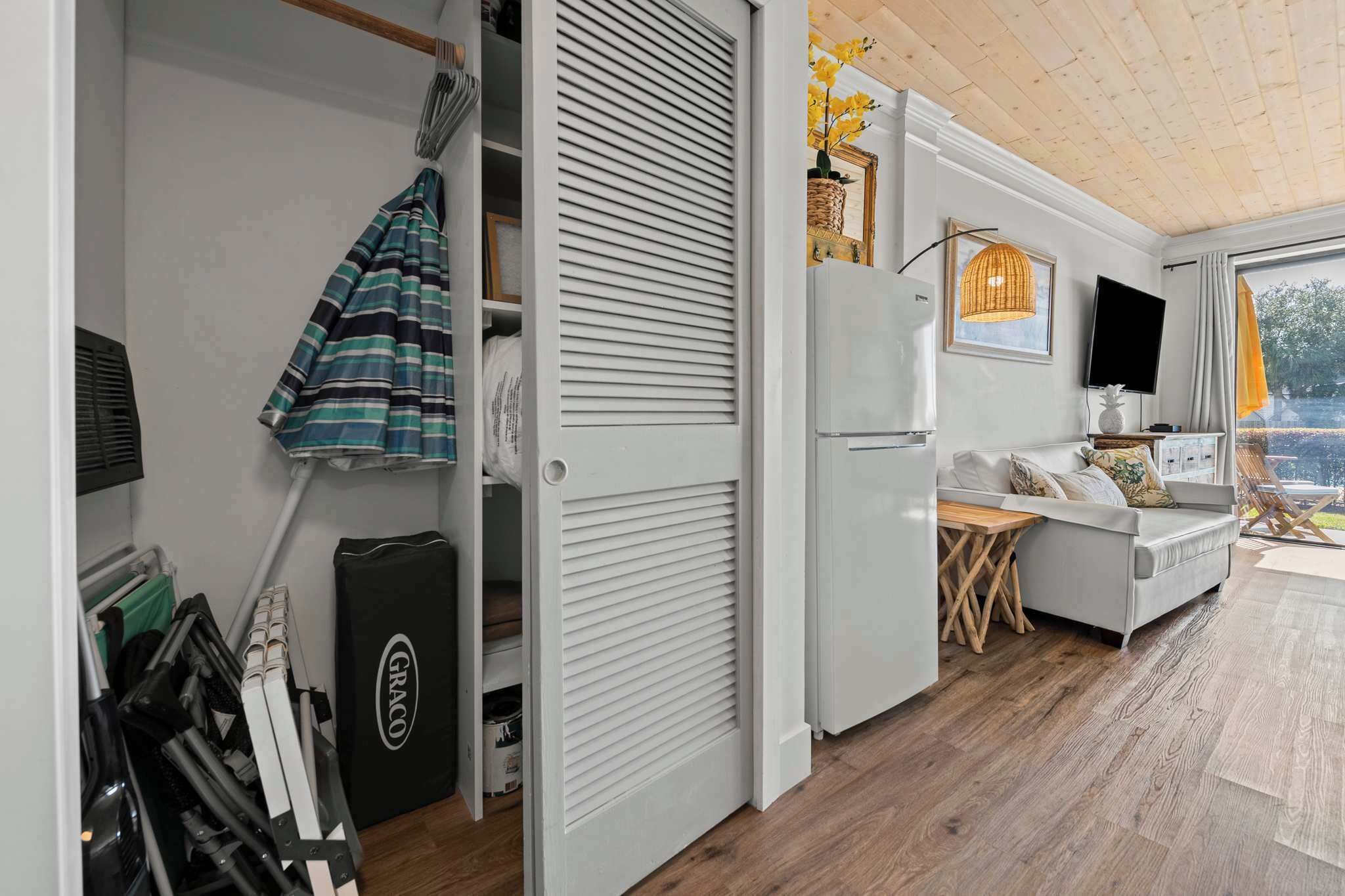 A room with a white wardrobe, a small table, a sofa, and a TV.