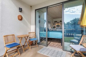 Un balcón con mobiliario de madera, un ventanal de vidrio que da a un dormitorio y vistas al exterior.