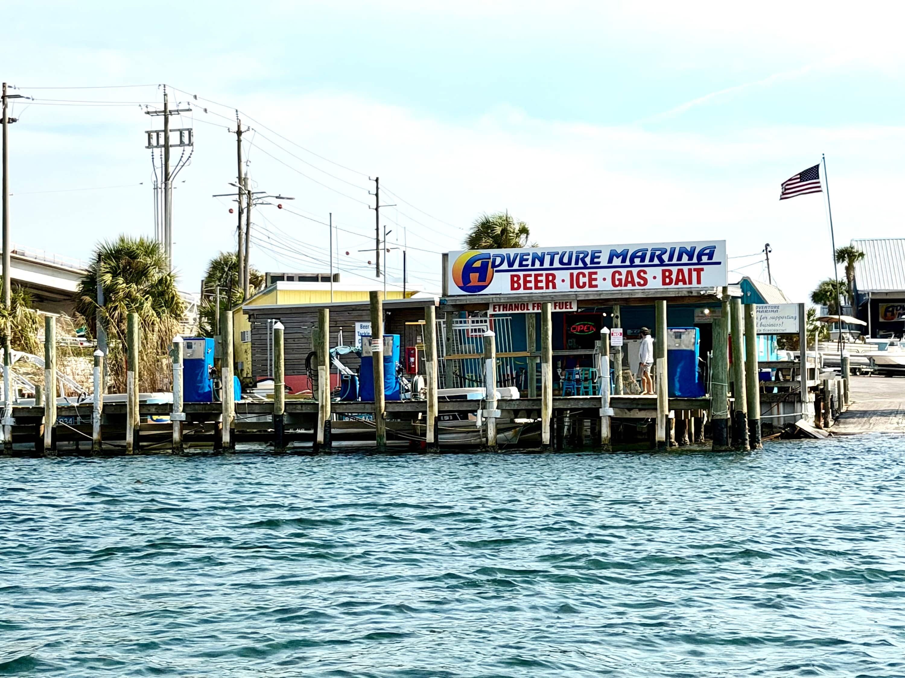 A waterfront establishment named 'Adventure Marina' with a signboard advertising beer, ice, gas, and bait.