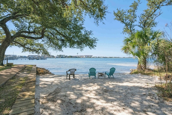 A beach with a wooden walkway, two green chairs, and a large tree providing shade. - Dockside Dream-Waterfront-Boat Slip-Downtown (Fort Walton Beach)