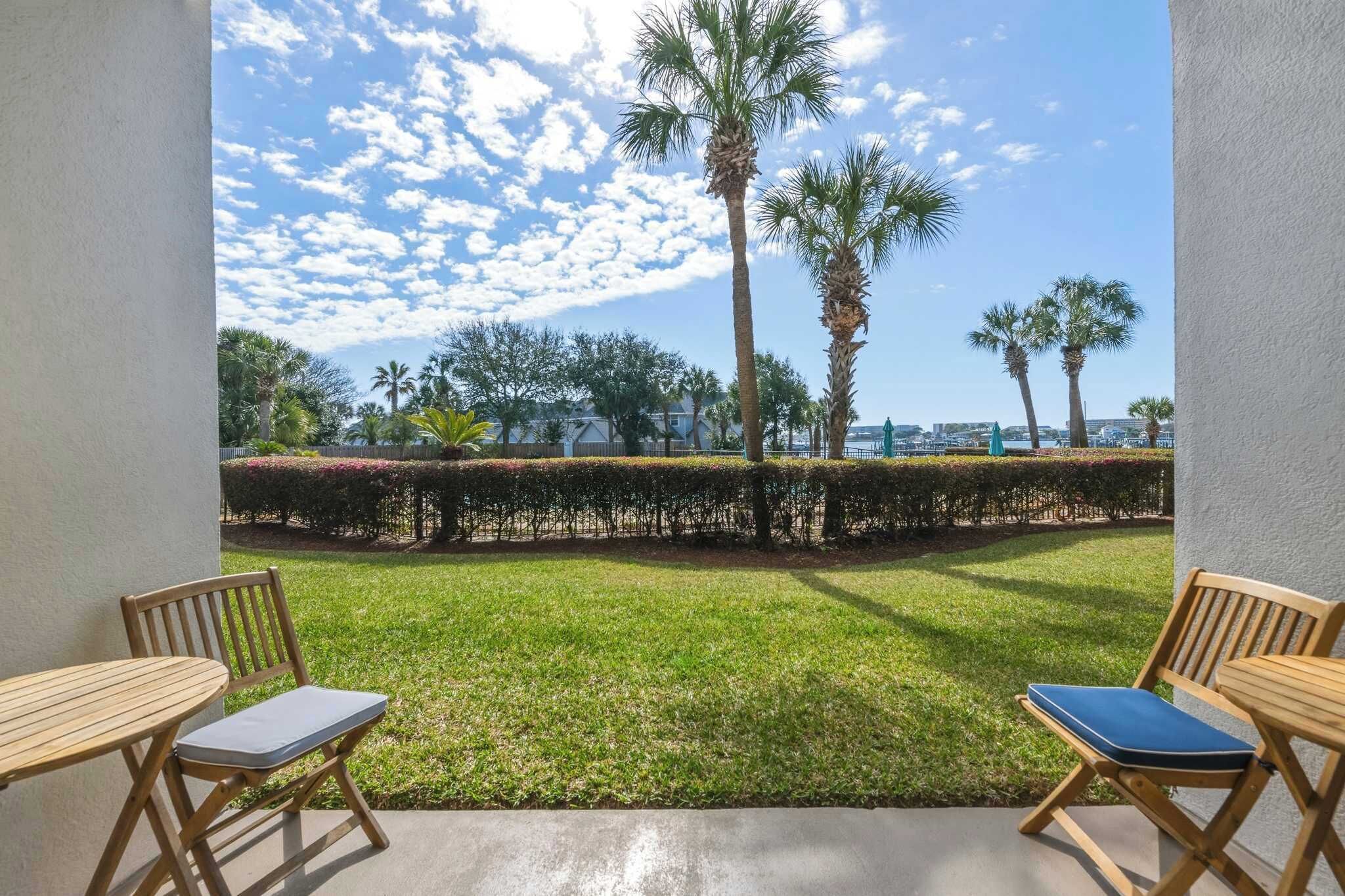 A patio with two wooden chairs and a table, a well-maintained lawn, and tall palm trees.