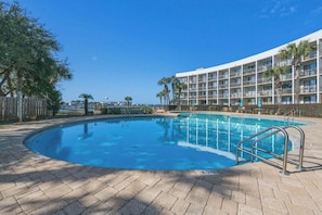 A swimming pool with a metal ladder, surrounded by a brick patio, and a multi-story hotel building in the background. - Dockside Dream-Waterfront-Boat Slip-Downtown (Fort Walton Beach)