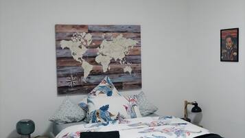 A bedroom with a bed, a nightstand, a lamp, a world map artwork, and a framed picture on the wall.