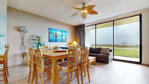 A spacious dining area with a wooden table and chairs, a ceiling fan, and a large window offering a view of the outdoors. - Ground-Floor Gulf-View 3BR: Suntide III - Unit 106 (South Padre Island)