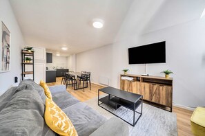 Ein modernes Wohnzimmer mit einem grauen Sofa, einem Holzschrank, einem Fernseher und einem Essbereich mit Stühlen und einem Tisch.