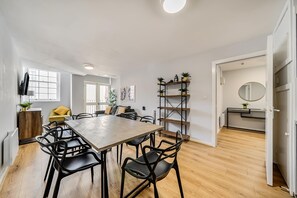 A modern kitchen with a wooden dining table, black chairs, and a yellow sofa. There are potted plants on shelves and a round mirror on the wall. - Host Stay Apartment 6 Stanley Street (Liverpool)