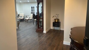 Un pasillo con piso de madera, un mueble negro con una planta y una gran silla de madera.