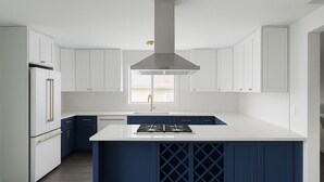 Una cocina moderna con armarios blancos, una isla central con estufa integrada y una campana extractora de acero inoxidable.
