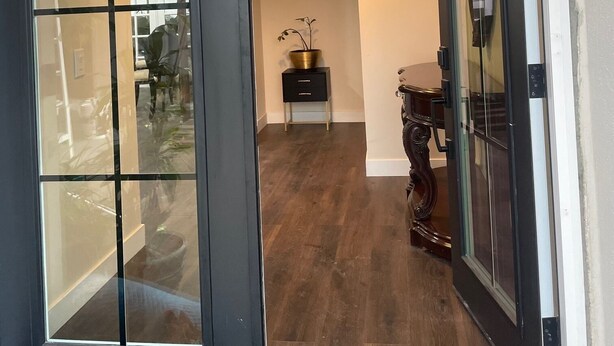 Un pasillo con suelo de madera, una puerta negra con paneles de vidrio y una pequeña mesa con una planta.