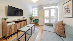 Un salon moderne avec un téléviseur à écran plat, un meuble de rangement en bois, une table basse en verre, un canapé gris et un fauteuil vert.