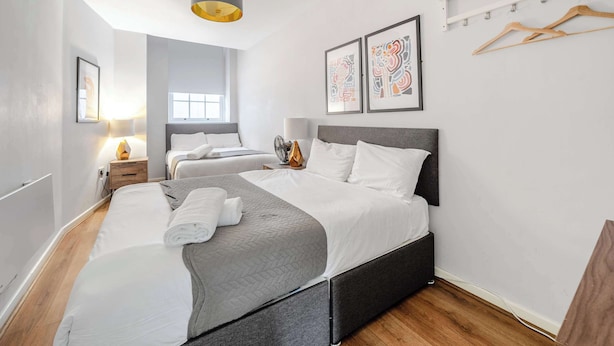 Une chambre d’hôtel moderne avec un grand lit, des tables de chevet, un luminaire au plafond et des œuvres d’art accrochées aux murs.