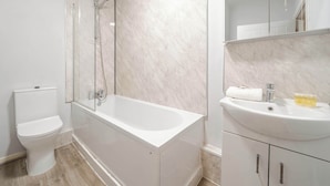 Une salle de bain moderne avec une douche à parois de verre, des toilettes blanches et un lavabo surmonté d’un miroir.