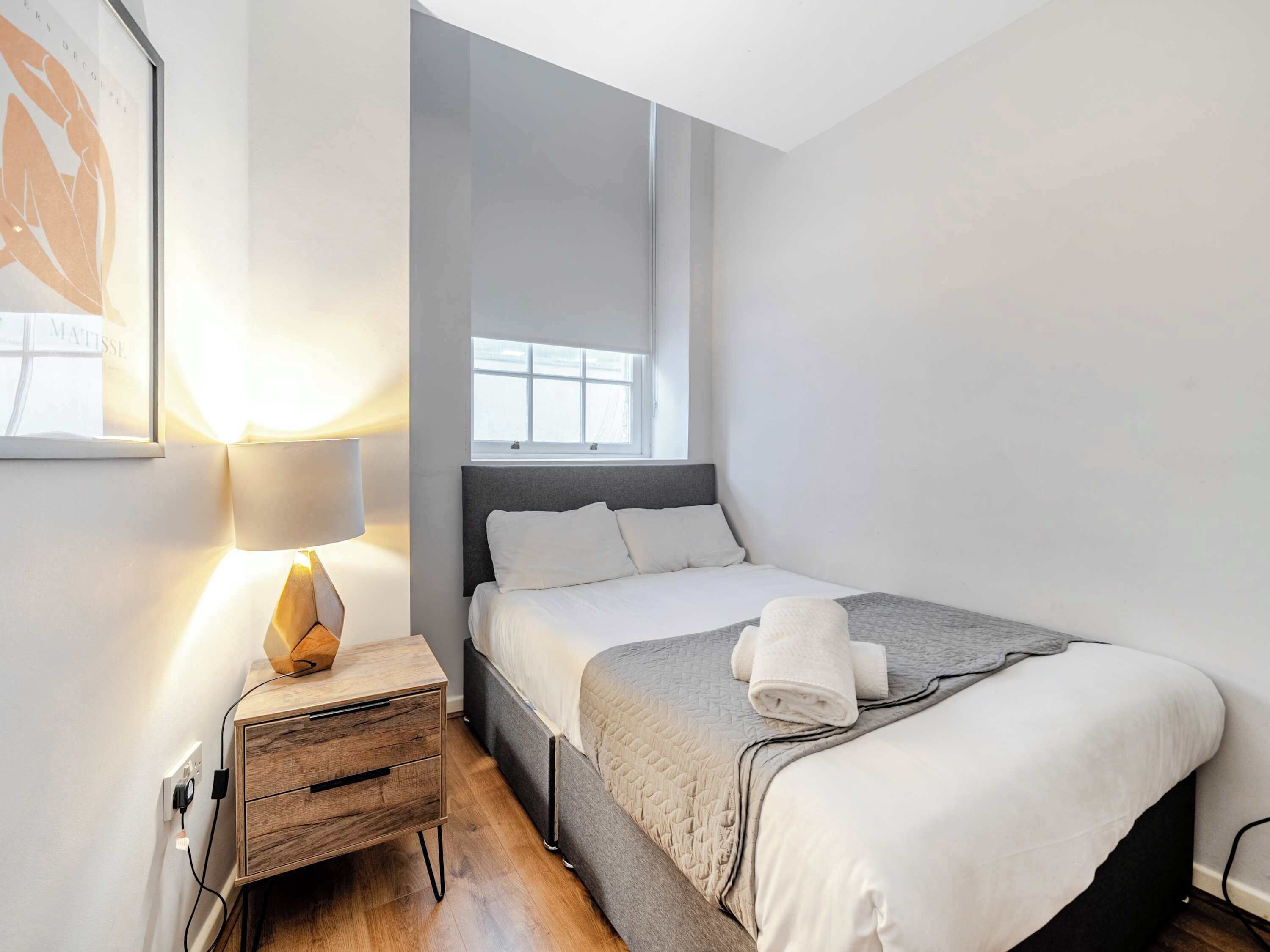A neatly arranged bedroom with a bed, bedside table, lamp, and a window.