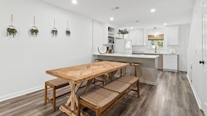 A modern kitchen with white cabinetry, a wooden dining table with benches, and hanging plants. - Townhouse Directly Across from Gulf- 2BR/2.5Ba (Panama City Beach)