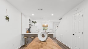 A modern kitchen with white cabinetry, a wooden dining table, and a unique white circular object on the table. - Townhouse Directly Across from Gulf- 2BR/2.5Ba (Panama City Beach)