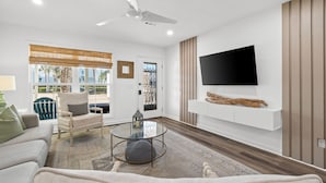 A modern living room with a sofa, armchair, glass coffee table, and a mounted TV. - Townhouse Directly Across from Gulf- 2BR/2.5Ba (Panama City Beach)