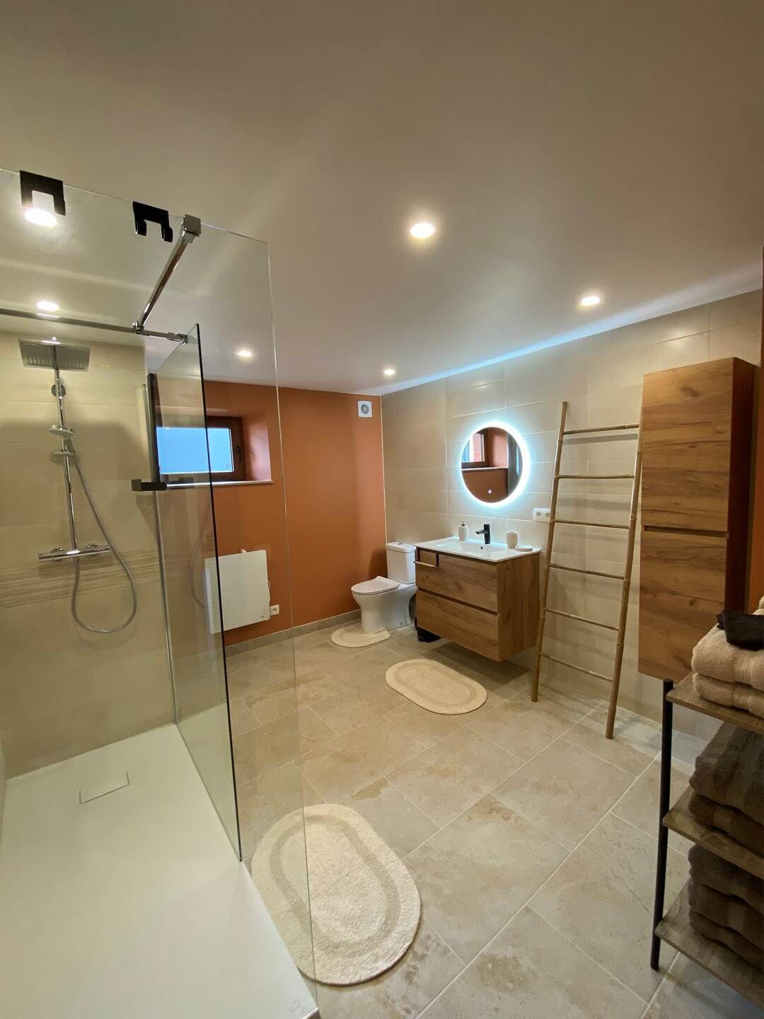 Ein modernes Badezimmer mit einer begehbaren Glasdusche, einem Holzwaschtisch, einer Toilette und einem Handtuchhalter.