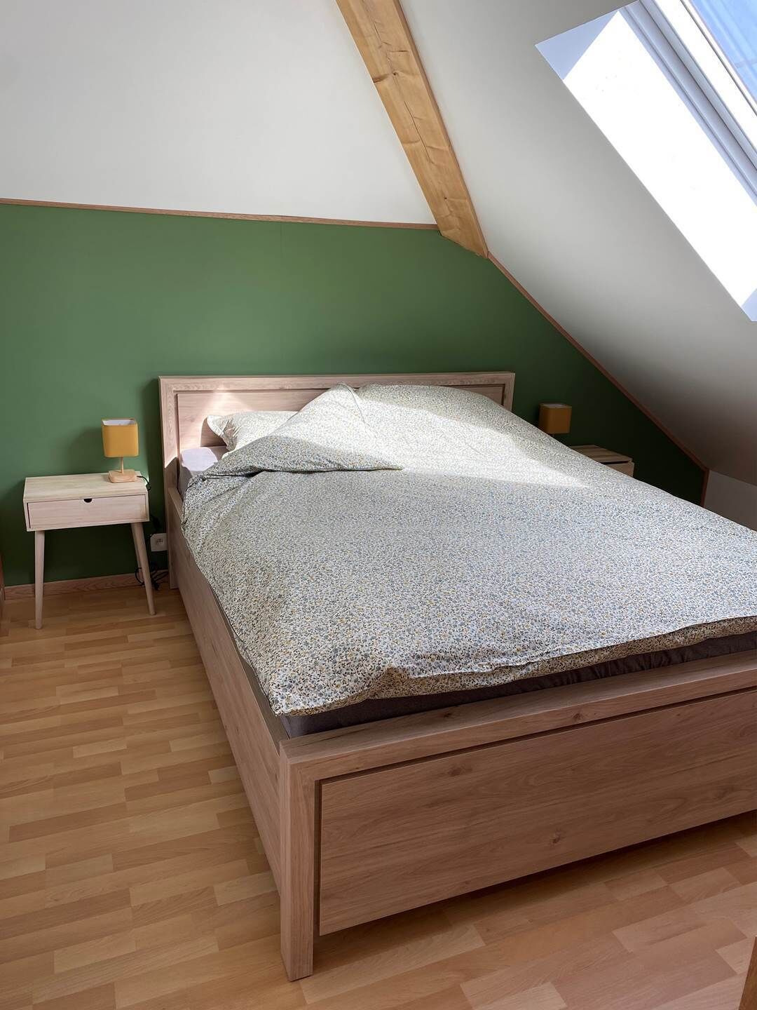 Ein Schlafzimmer mit schrägem Dach, einem hölzernen Bett, zwei Nachttischen mit Lampen und einer grünen Wand.