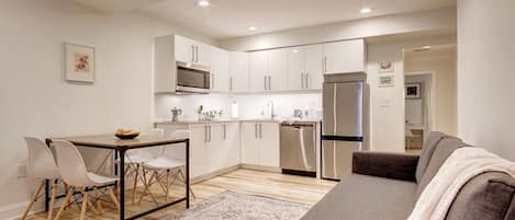 A modern kitchen with white cabinets, stainless steel appliances, and a dining area with a table and chairs.