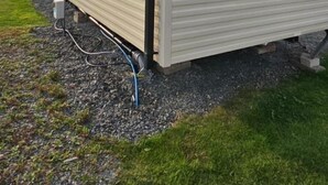 A single-story mobile home with a flat roof, large windows, and a visible electrical outlet on the ground. - Willerby Seasons: 3BR Caravan (Morecambe)