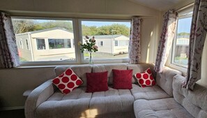 A sofa with four red pillows and a vase with flowers on a windowsill. - Willerby Seasons: 3BR Caravan (Morecambe)