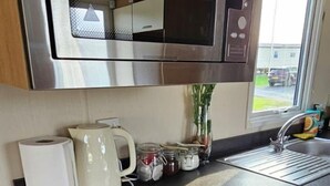 A compact kitchenette with a stainless steel microwave, a kettle, a sink, and a small countertop. - Willerby Seasons: 3BR Caravan (Morecambe)