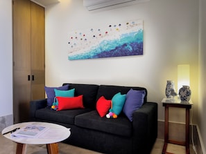 Een moderne woonkamer met een zwarte bank, kleurrijke kussens, een ronde salontafel en een abstract schilderij aan de muur.