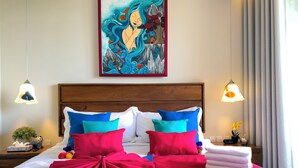 Un lit bien fait, agrémenté de coussins colorés, une grande peinture au-dessus et deux lampes de chevet.