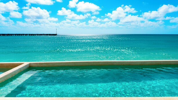 Helderblauwe lucht, turkoois water en een steiger die het water in reikt.