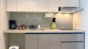 A modern kitchen with white cabinets, a coffee maker, a sink, and a trash bin. - Casa la Aurora (Puerto Morelos)