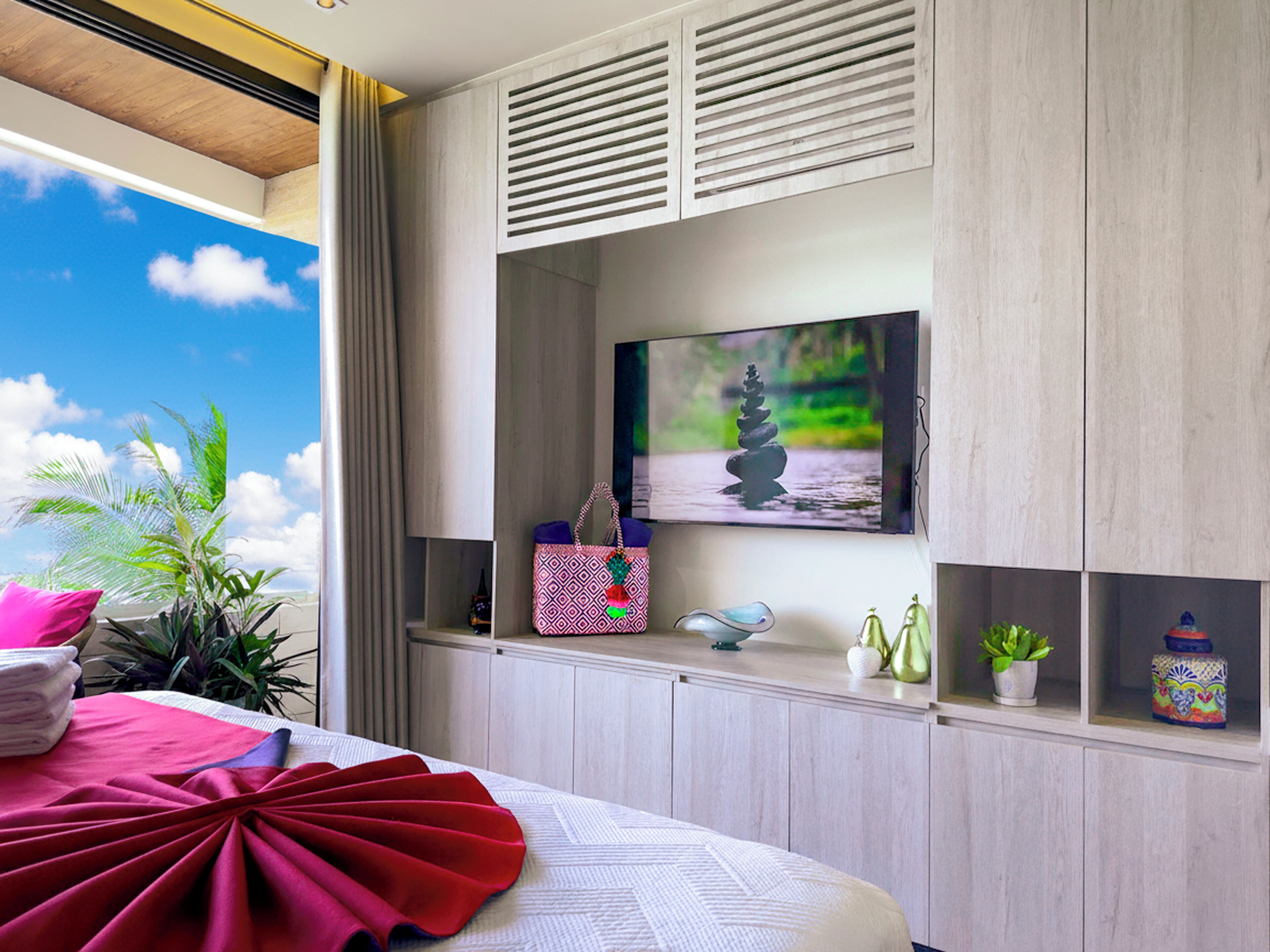 Een moderne slaapkamer met een bed, een aan de muur bevestigde televisie en een raam met uitzicht op de lucht.