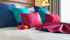 A bed with multiple pillows in various colors, a white textured bedspread, and a lamp in the background. - Casa la Aurora (Puerto Morelos)