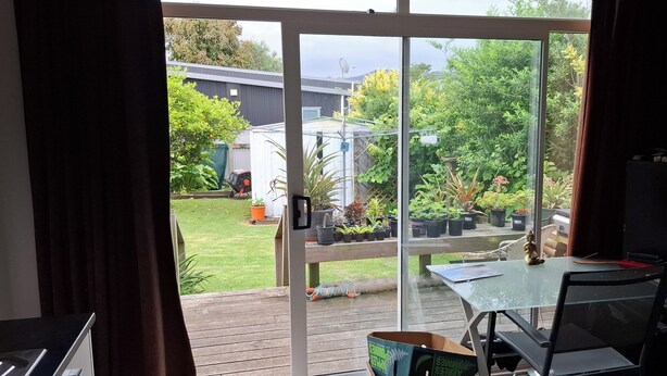 A room with a glass door leading to a garden area with potted plants and a wooden deck.