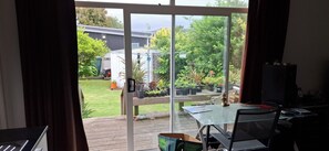 Ein Zimmer mit Glastür, das zu einem Gartenbereich mit Topfpflanzen und einer Holzterrasse führt.