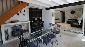 Un salon moderne avec une table à manger en verre, des chaises noires, un escalier en bois et un mur en pierre.