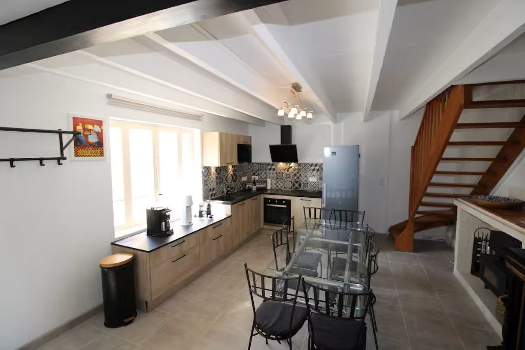 A modern kitchen with a glass dining table, wooden cabinets, and a built-in oven.
