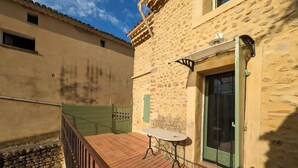 Une terrasse avec une table et des chaises, un mur en pierre et une porte avec un volet vert.