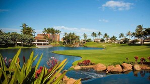 A golf course with a pond, palm trees, and a building in the background. - Luxury Oasis Resort Villa (Kapolei)
