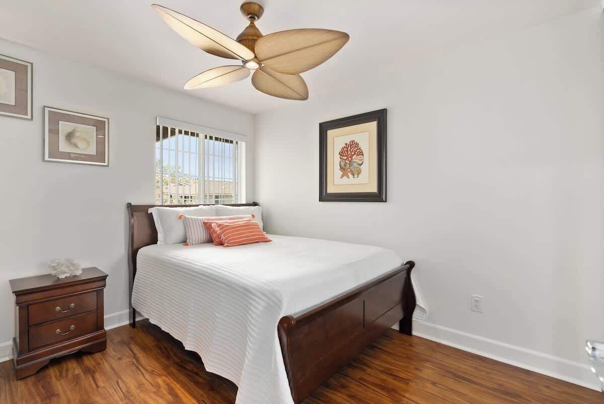 Une chambre à coucher comprenant un lit, une table de chevet, un ventilateur de plafond et des œuvres d’art encadrées accrochées aux murs.