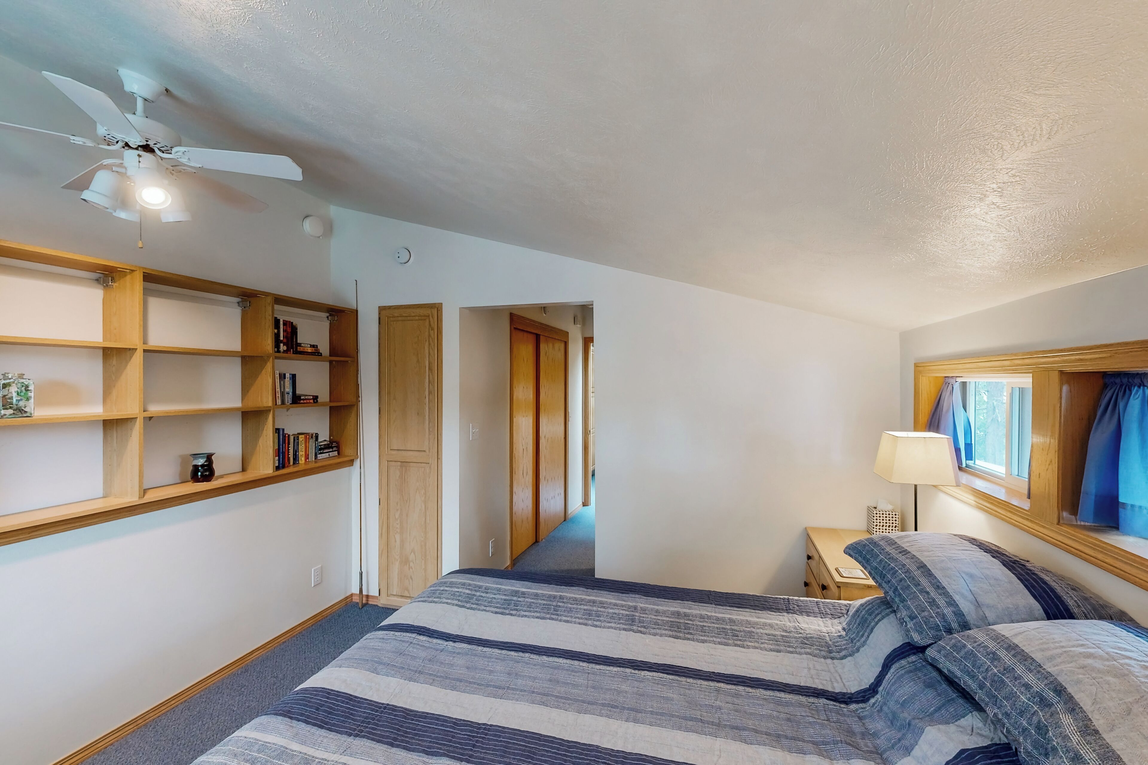 Une chambre à coucher avec un lit, des étagères en bois, un ventilateur de plafond et une table de chevet.