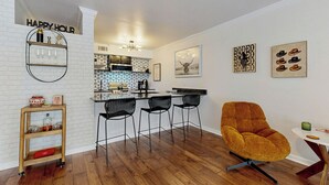 A modern kitchen with a bar area, a wooden dining table with chairs, and a vibrant orange chair. - ‘Lakeside Getaway’ w/ Patio on Lady Bird Lake (Austin)