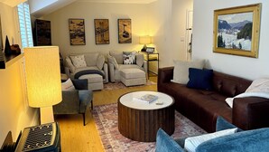A living room with a sofa, armchairs, a coffee table, and a lamp. There are paintings on the wall and a door in the background. - Quiet Village Gem! Cozy retreat for two. (Stowe)