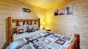 Ein Schlafzimmer einer Holzhütte mit einem Bett, Nachttischen und Wandbildern.