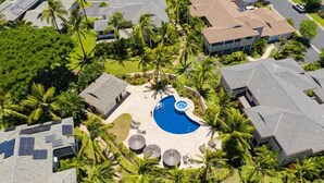 Ett flygbildsbild av ett bostadsområde med en central pool omgiven av palmer och hus med sluttande tak.