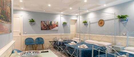 A hotel room with a large bed, a small table, two chairs, a wall-mounted plant, and a ceiling fan.